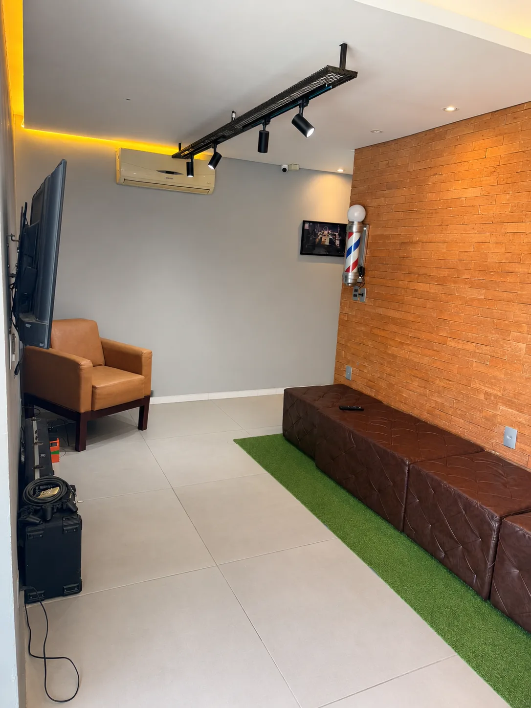 Lounge de espera da Mutari Barbershop com parede de tijolinho e barber pole